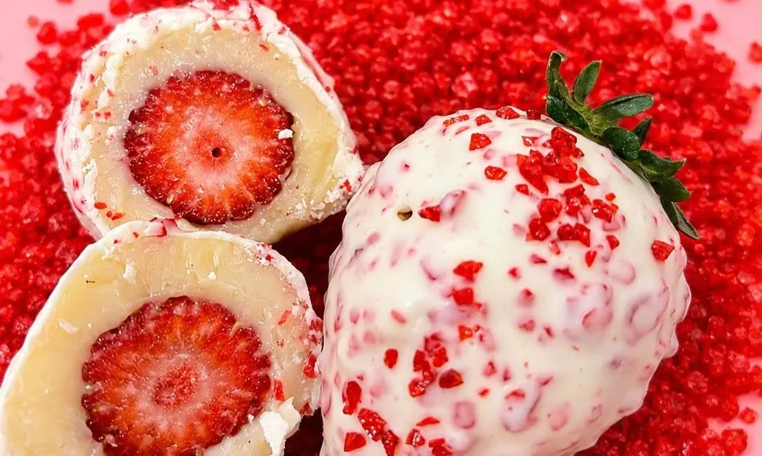 Conhecido como morango cravejado, o doce mant&eacute;m a combina&ccedil;&atilde;o de morango e brigadeiro branco, mas recebe uma cobertura diferente. | Foto: @deliciasdabiaofc